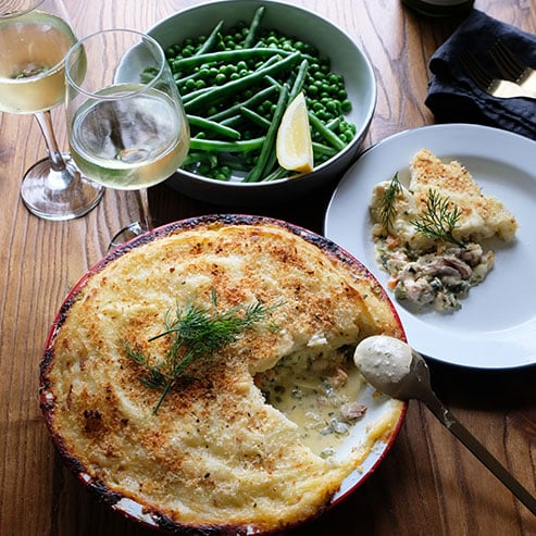 Creamy fish pie with two glasses of white wine and beans
