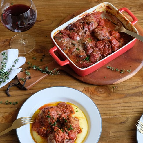 Red dish of meatballs, garnished with thyme and a plate of meatballs alongside a glass of tempranillo