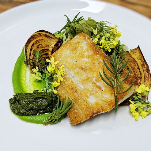 Seared Kingfish dish with flower garnish on a table with a grey table cloth