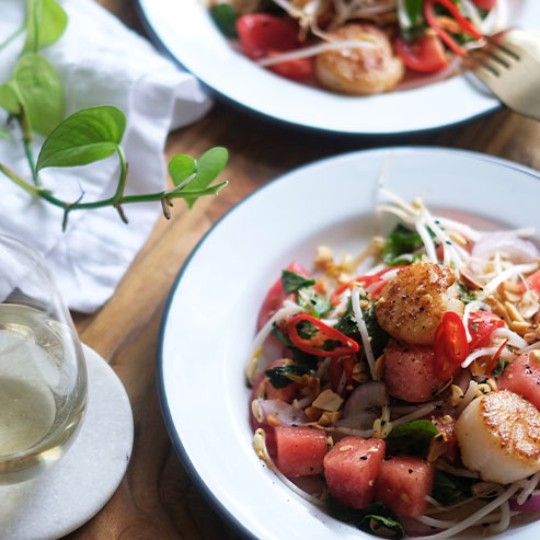 Two plates of seared scallop salad with a glass of sauvignon blanc