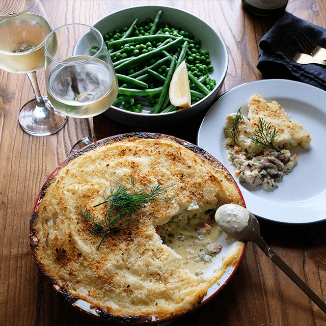 Creamy fish pie served with white wines beans and peas