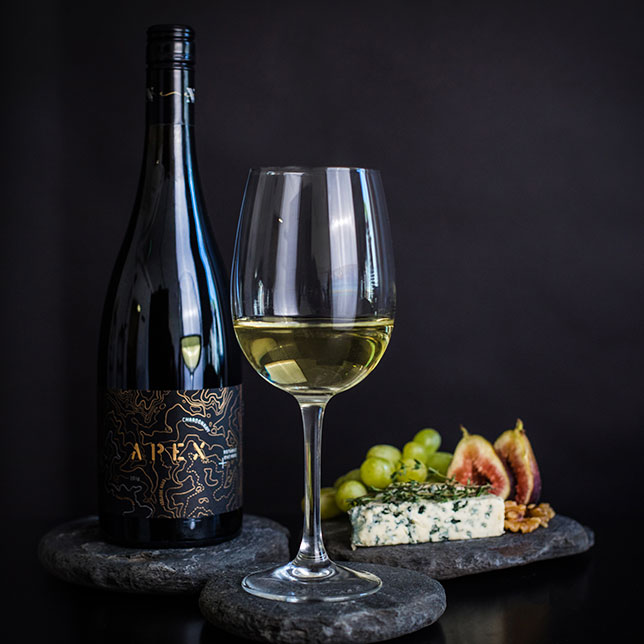 Bottle and glass of Nepenthe Apex Chardonnay next to blue cheese and figs