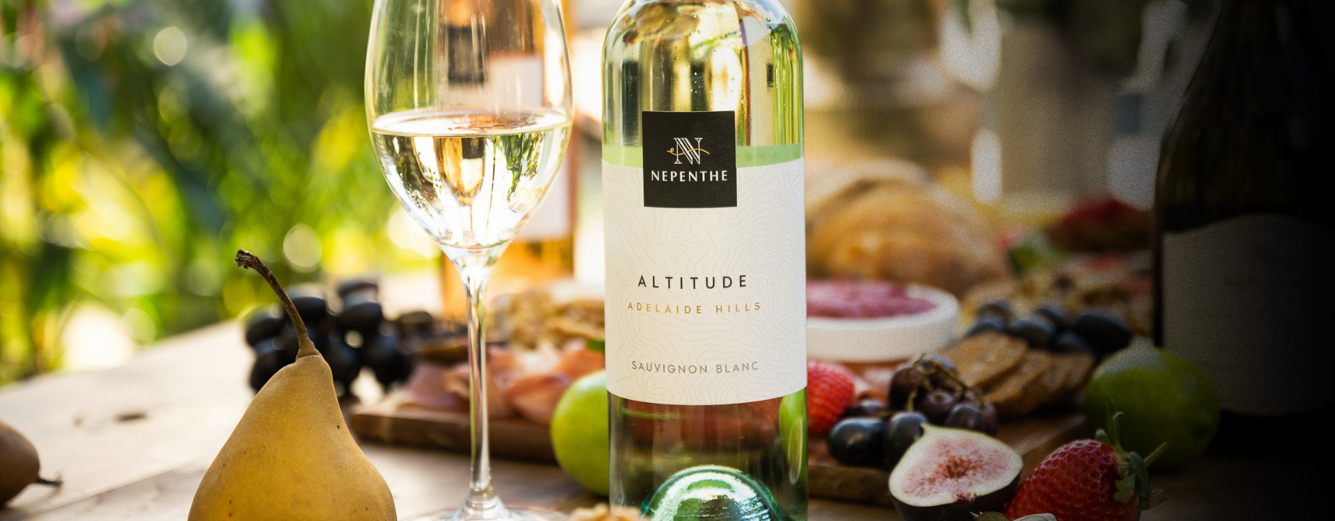 Nepenthe Altitude 2021 Sauvignon Blanc Bottle of wine on a table with fruit scattered.