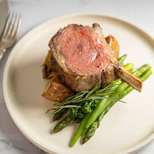 Plate of standing rib roast with asparagus and thyme and cutlery