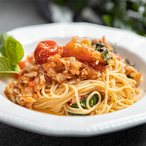 Bowl of chili crab pasta with mint leaves and a cherry tomato