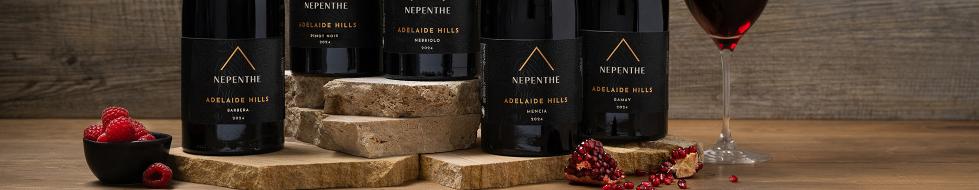 Bottles of Nepenthe Pinnacle varietals with a small bowl of raspberries and pomegranate seeds scattered.