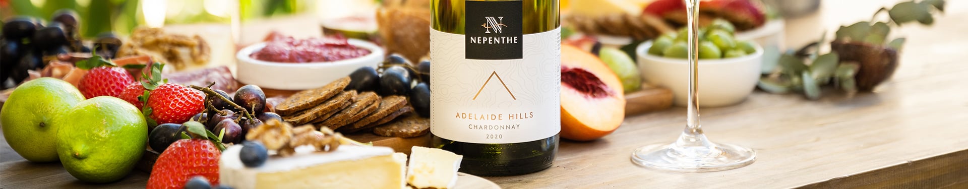 Bottle of Nepenthe Elevation 2020 Chardonnay surrounded by a charcuterie board containing fruit, meat and cheese