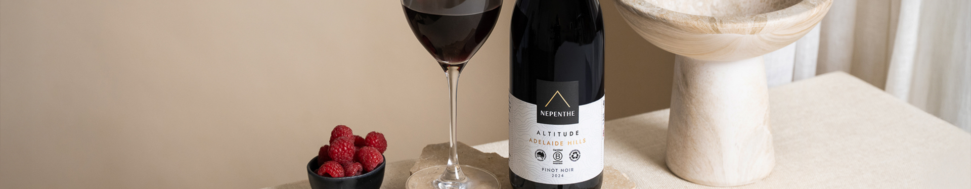 Bottle of Pinot Noir Altitude with a vase and a bowl of raspberries.
